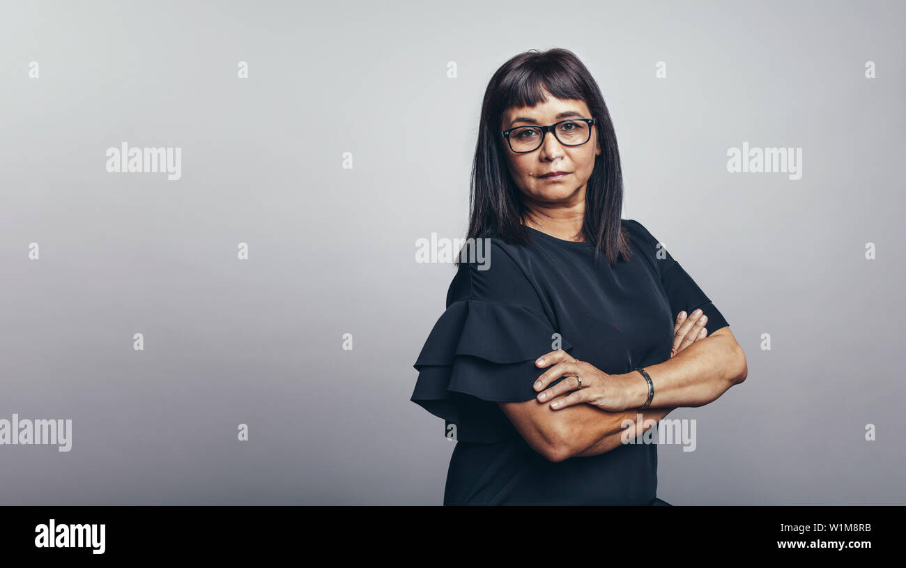 Woman standing against grey background looking at camera. Middle aged woman standing with her arms crossed. Stock Photo