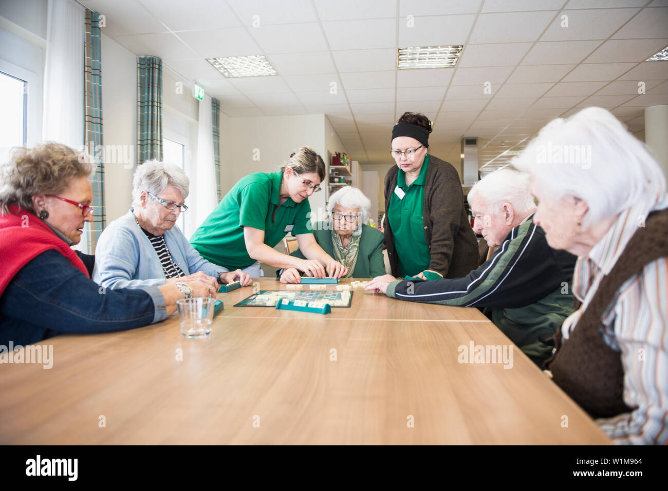 Senior inhabitants playing board game with nurse in rest home Stock Photo