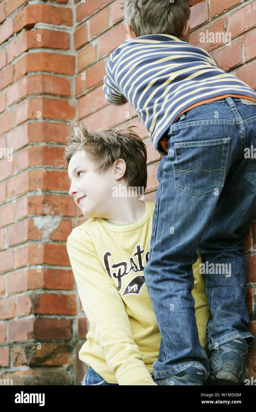 Two boys climbing over a wall Stock Photo