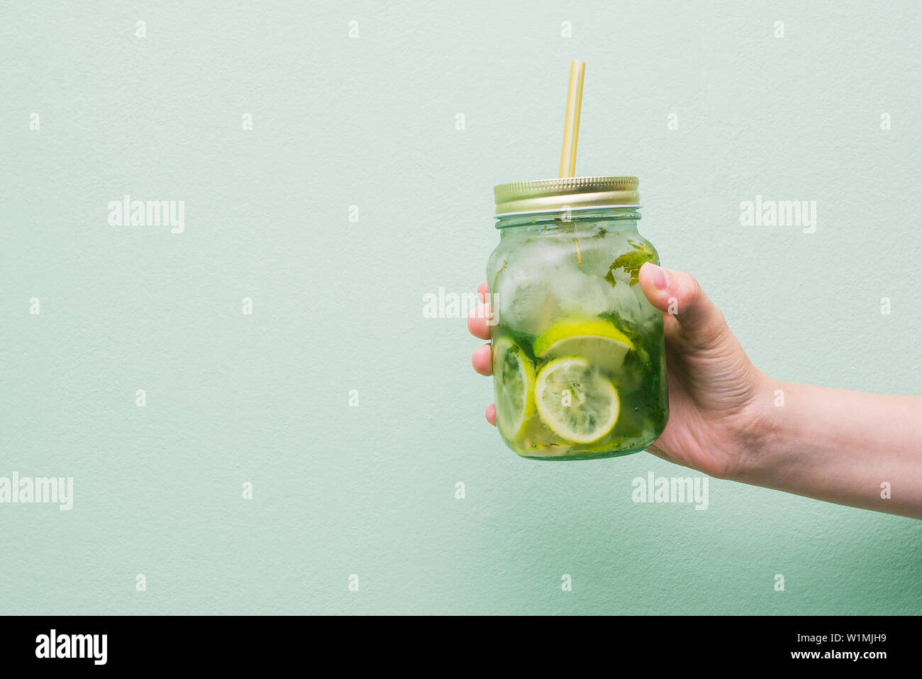 Summer refreshing cocktail in the hands of the girl. Cold drink mojito, with a striped tubule. Fruit non-alcoholic beverage in a glass jar Stock Photo