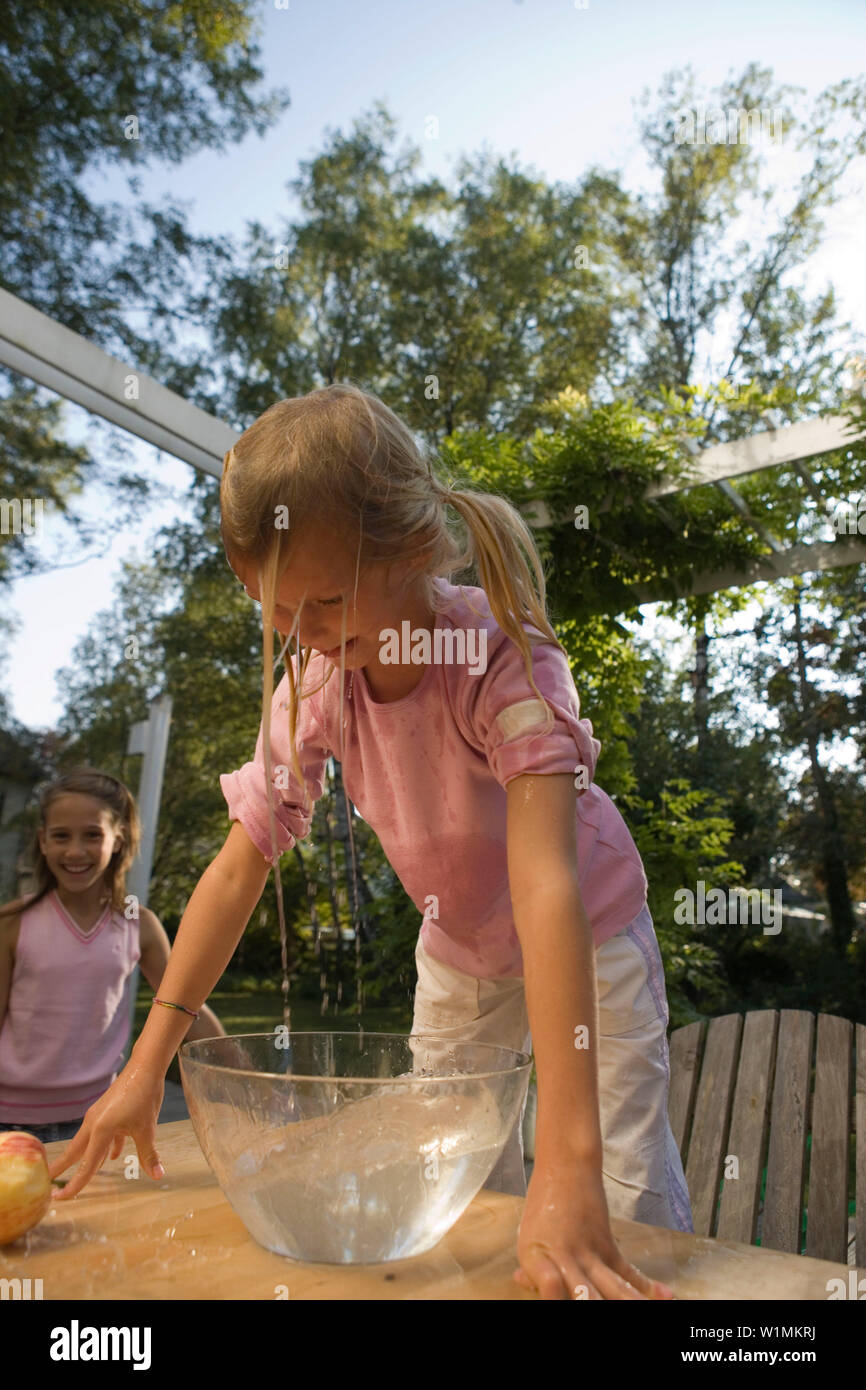 Wet girl bending over a dish with water and an apple, children's birthday party Stock Photo