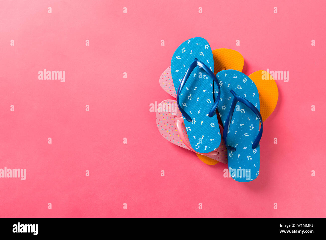 A lot of colored flip flops on pink background. Top view with copy ...