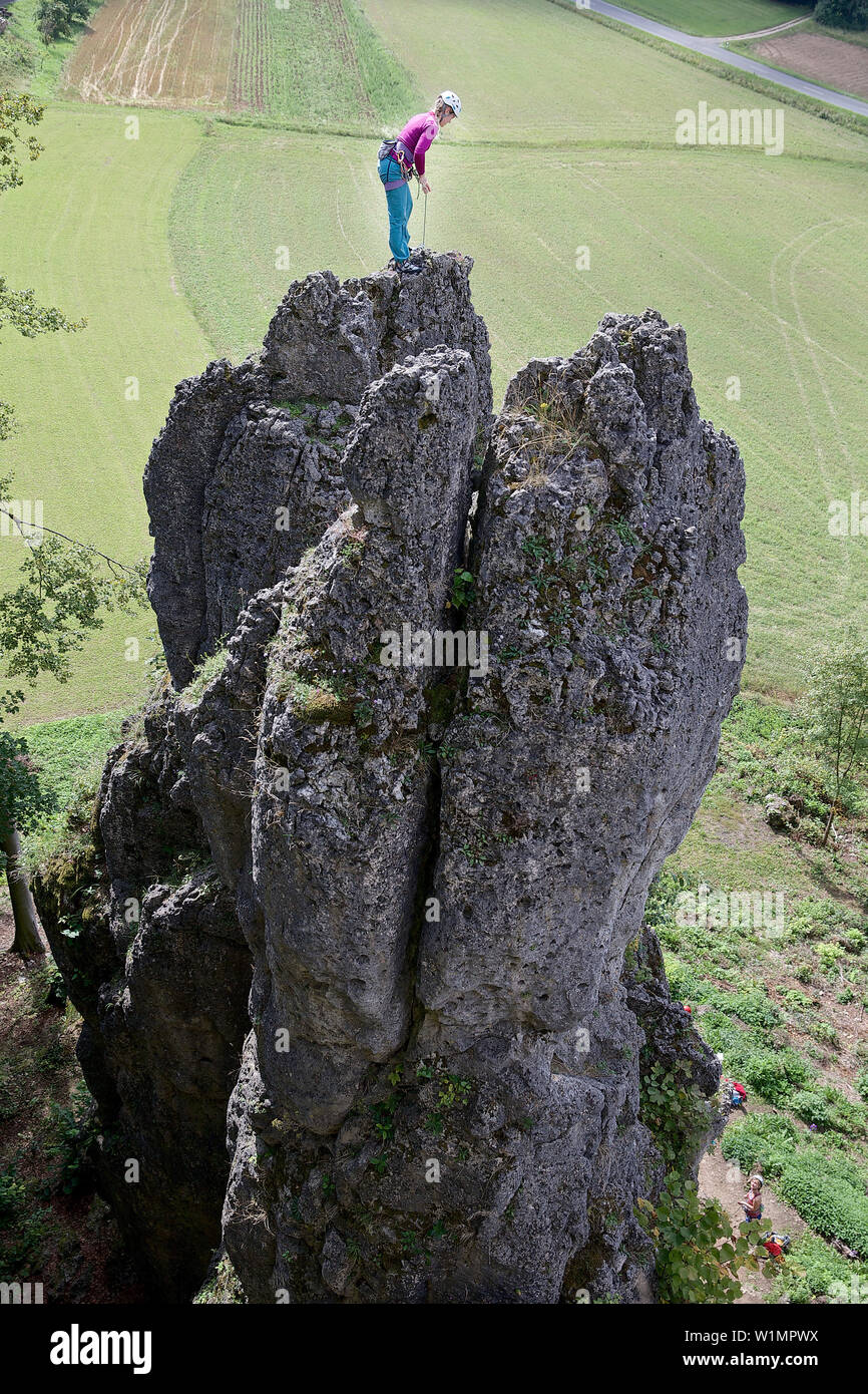 Young female climber standing on the top of a high rock, Pottenstein, Franconia, Germany Stock Photo