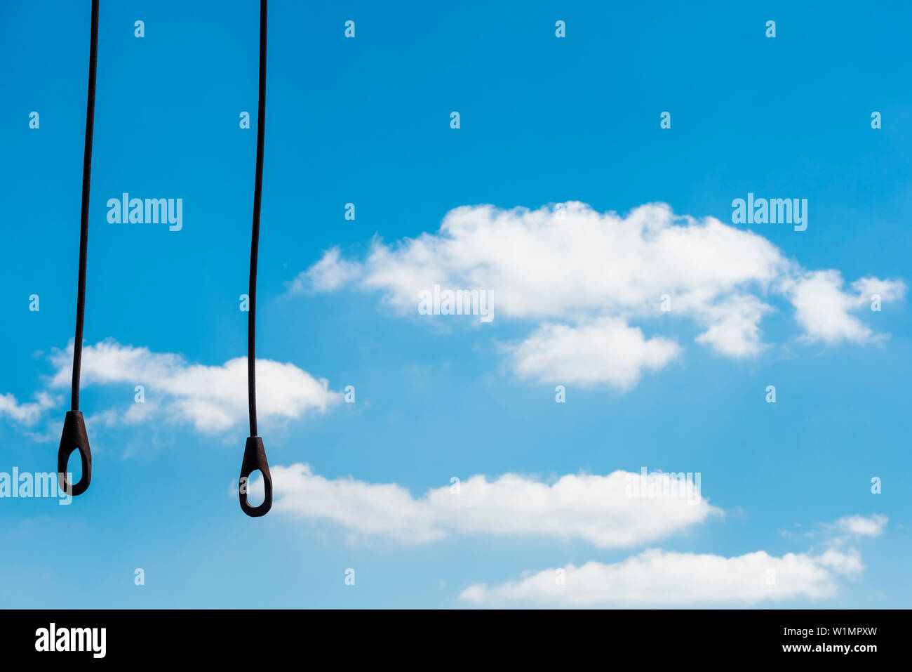Steel ropes with hooks hang from a crane in front of blue sky with cumulus clouds, Hamburg, Germany Stock Photo
