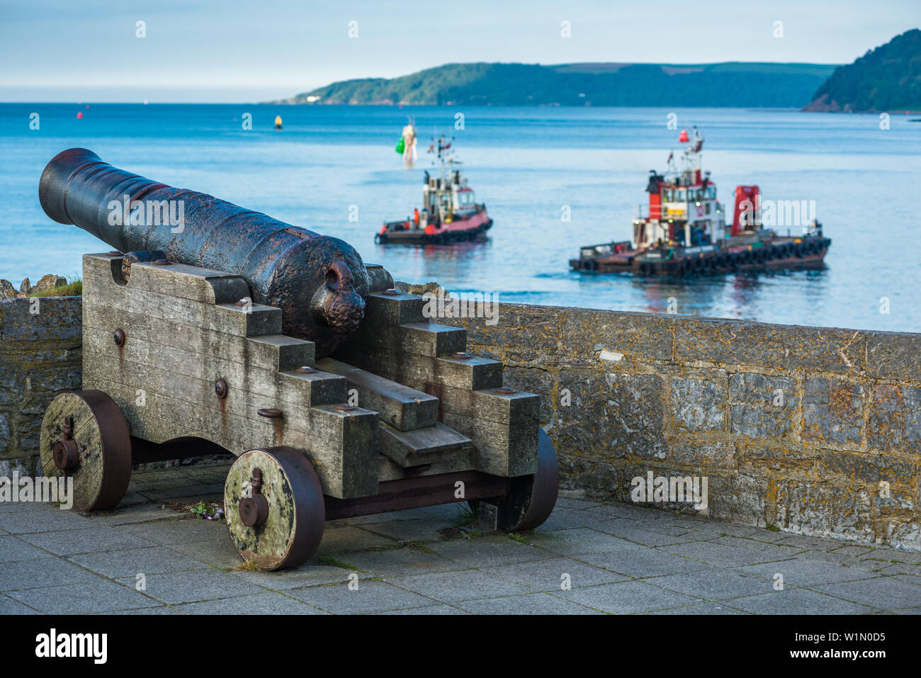 A restored 19th century Blomefield design cast iron cannon points across the water as boats passby, on Plymouth seafront in south Devon, UK Stock Photo