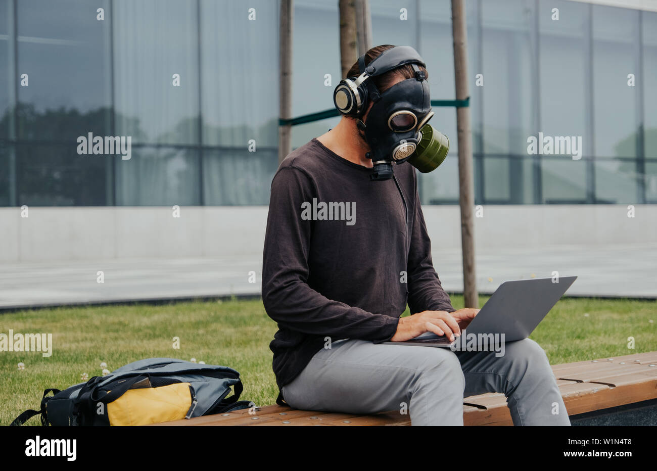 A city man in a gas mask works and listens to music against the background of a building and trees in a vacuum without people Stock Photo