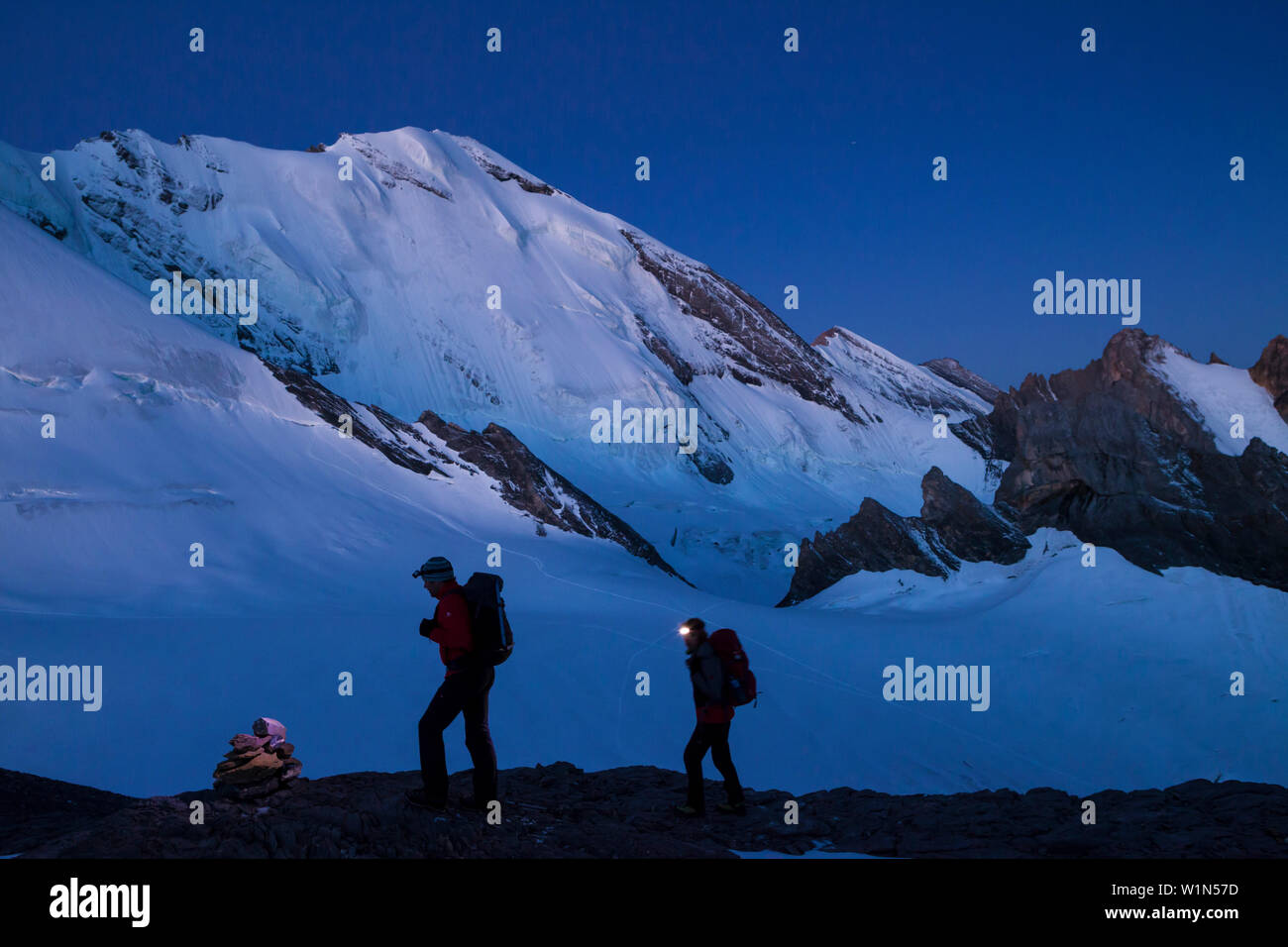 A man and a woman hiking with head torches, ascent at dawn to the summit of Mount Wildi Frau, view towards Bluemlisalp mountains, Bluemlisalphorn, Ber Stock Photo