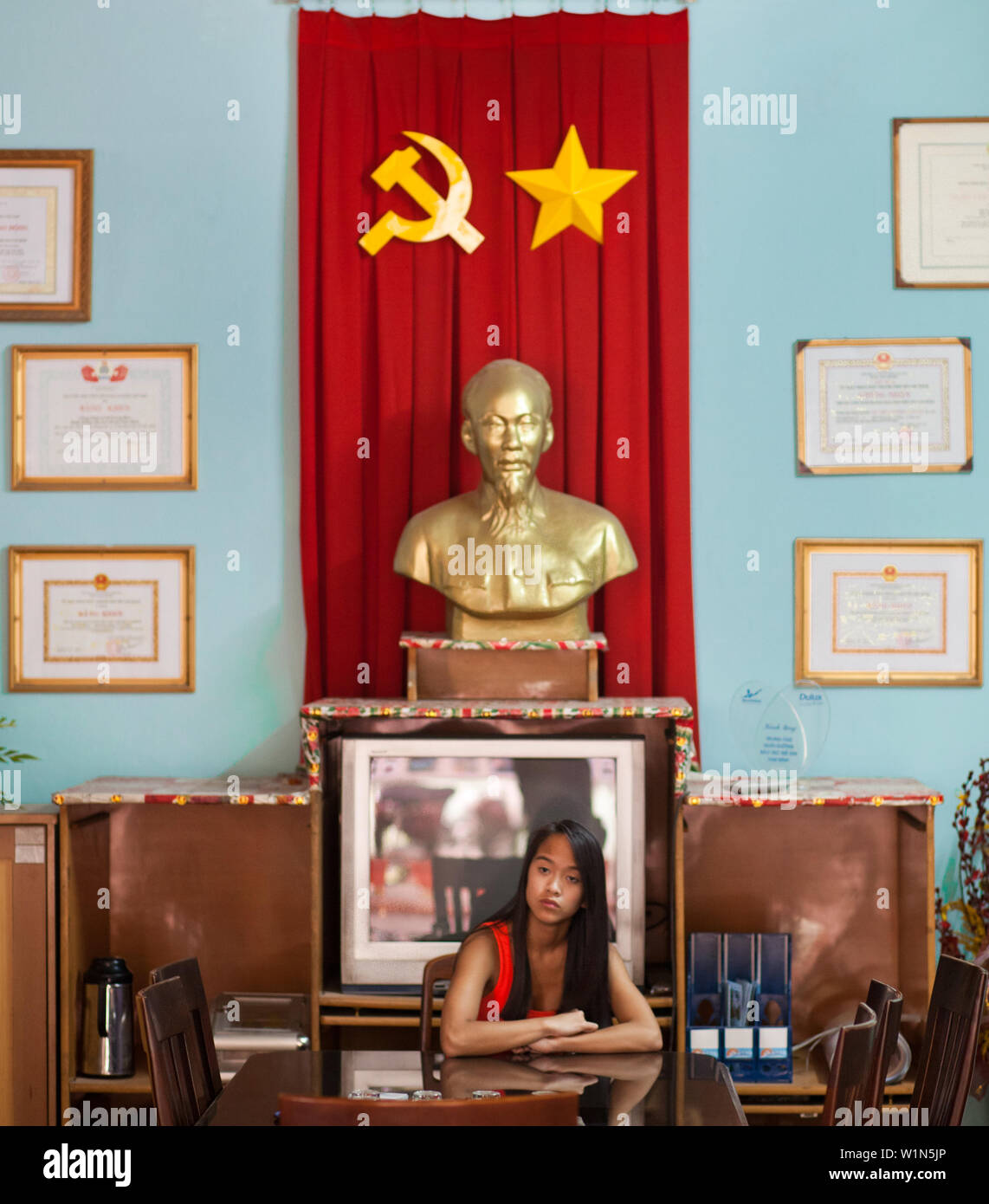 13 year old  girl in  south Vietnam, Ho Chi Minh City sits in front of a statue of  Ho Chi Minh and symbols of communism Stock Photo
