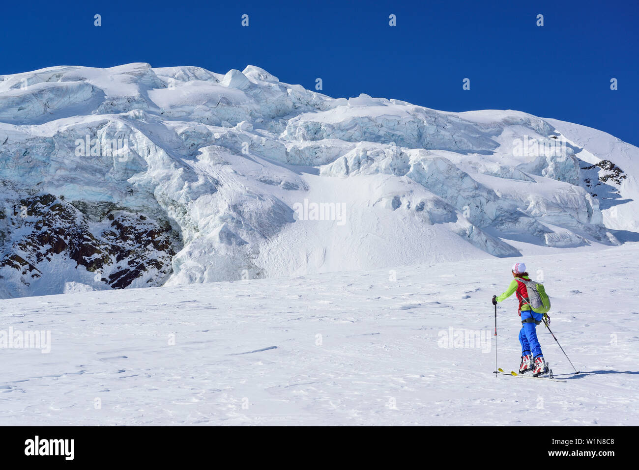 Woman back-country skiing ascending towards icefall, Punta San Matteo, Val dei Forni, Ortler range, Lombardy, Italy Stock Photo