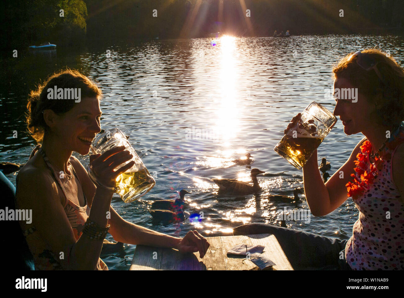 Young women toasting with beer steins, Seehaus Beergarden, English Garden, Munich, Bavaria, Germany Stock Photo