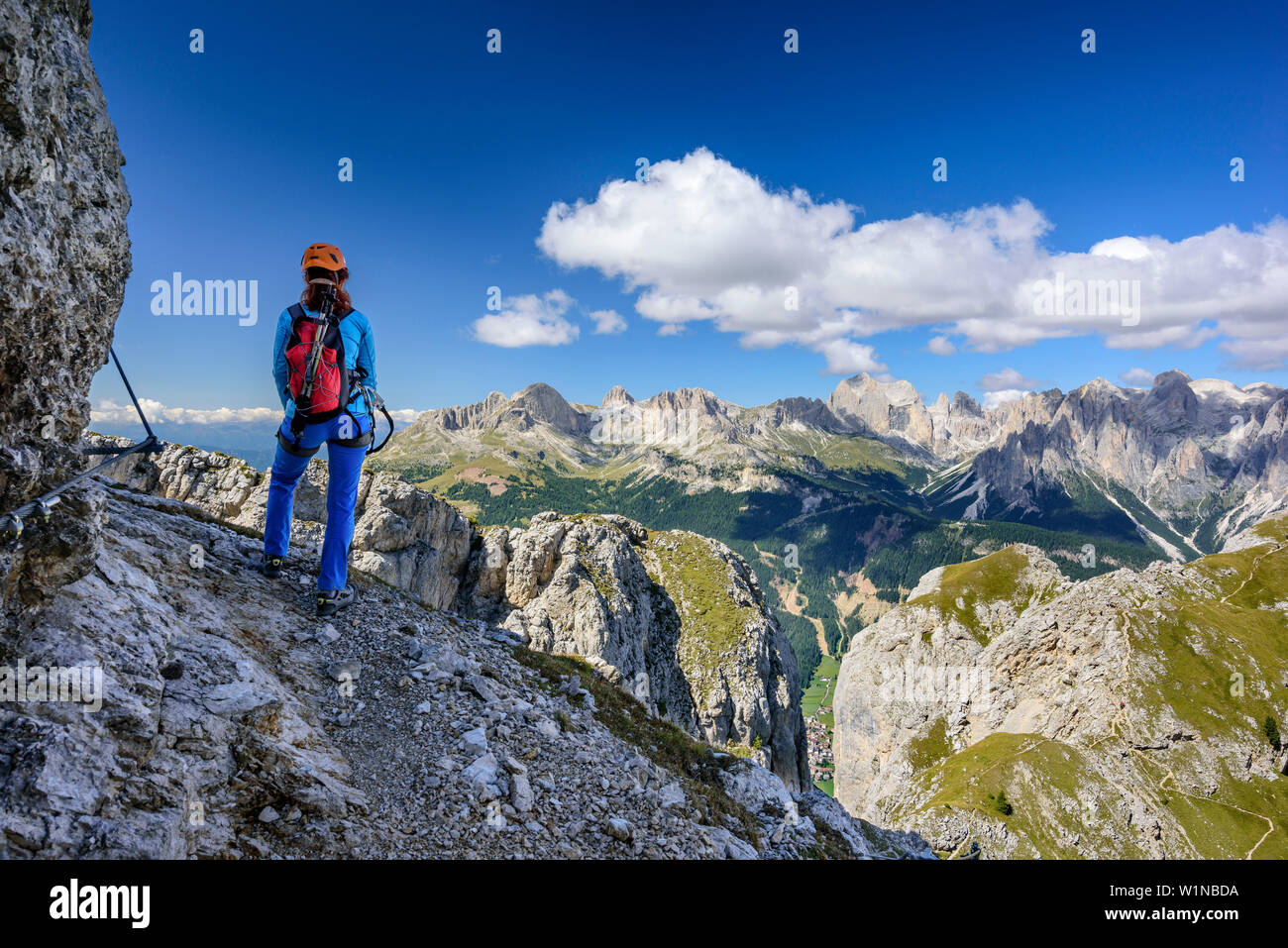 Woman ascending on fixed rope route looking towards Rosengarten range, Sas Aut, Vallaccia range, Marmolada, Dolomites, UNESCO World Heritage Dolomites Stock Photo