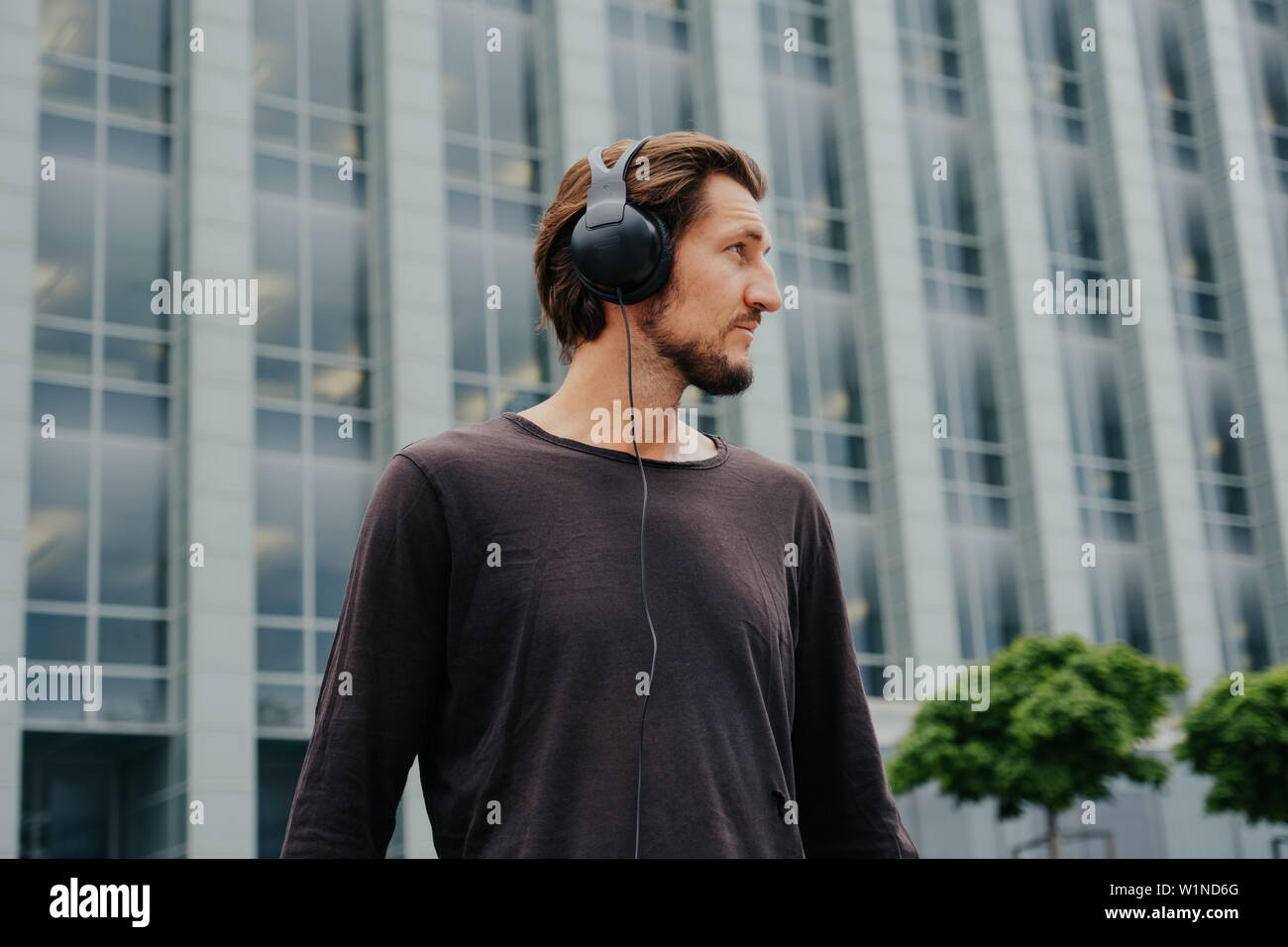 The freelance guy listens to music on headphones, backpac and works on a laptop in the center of a big city. Stock Photo