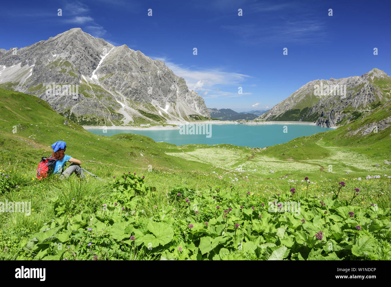 Woman hiking sitting in meadow and looking towards lake Luenersee, lake Luenersee, Raetikon trail, Raetikon, Vorarlberg, Austria Stock Photo