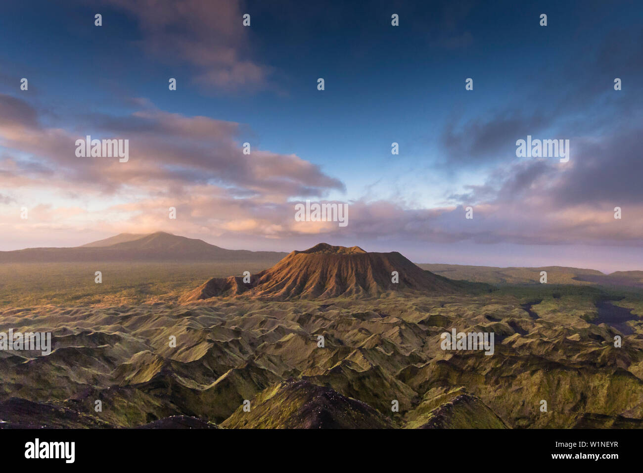 Extinct volcano crater in the evening light. Flanks and surroundings are overgrown with vegetation. Blue Hour, clouds are illuminated by the setting s Stock Photo