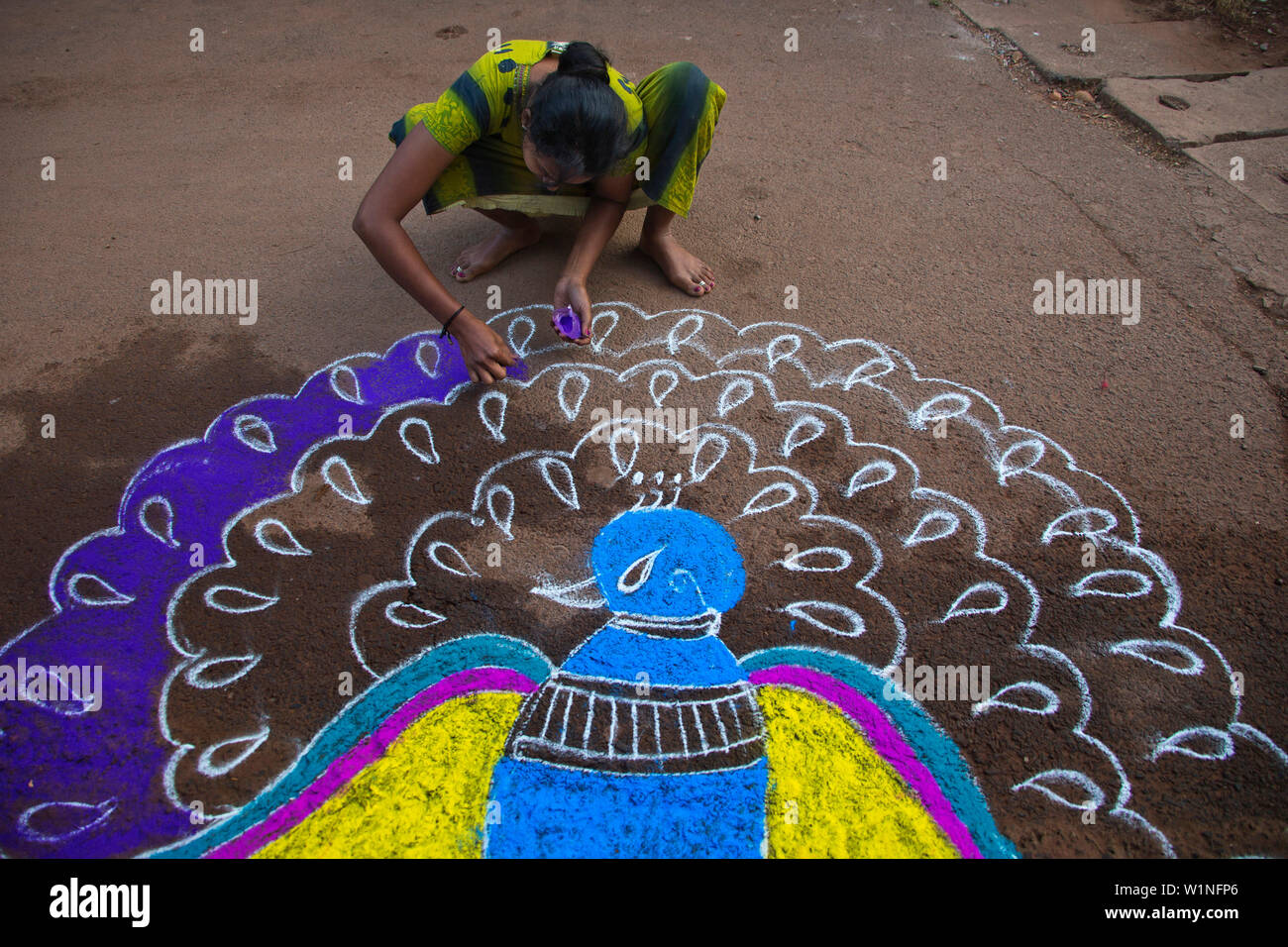 A young Indian female painting a peacock on the street in celebration of a festival, Betul Beach, Goa, India Stock Photo