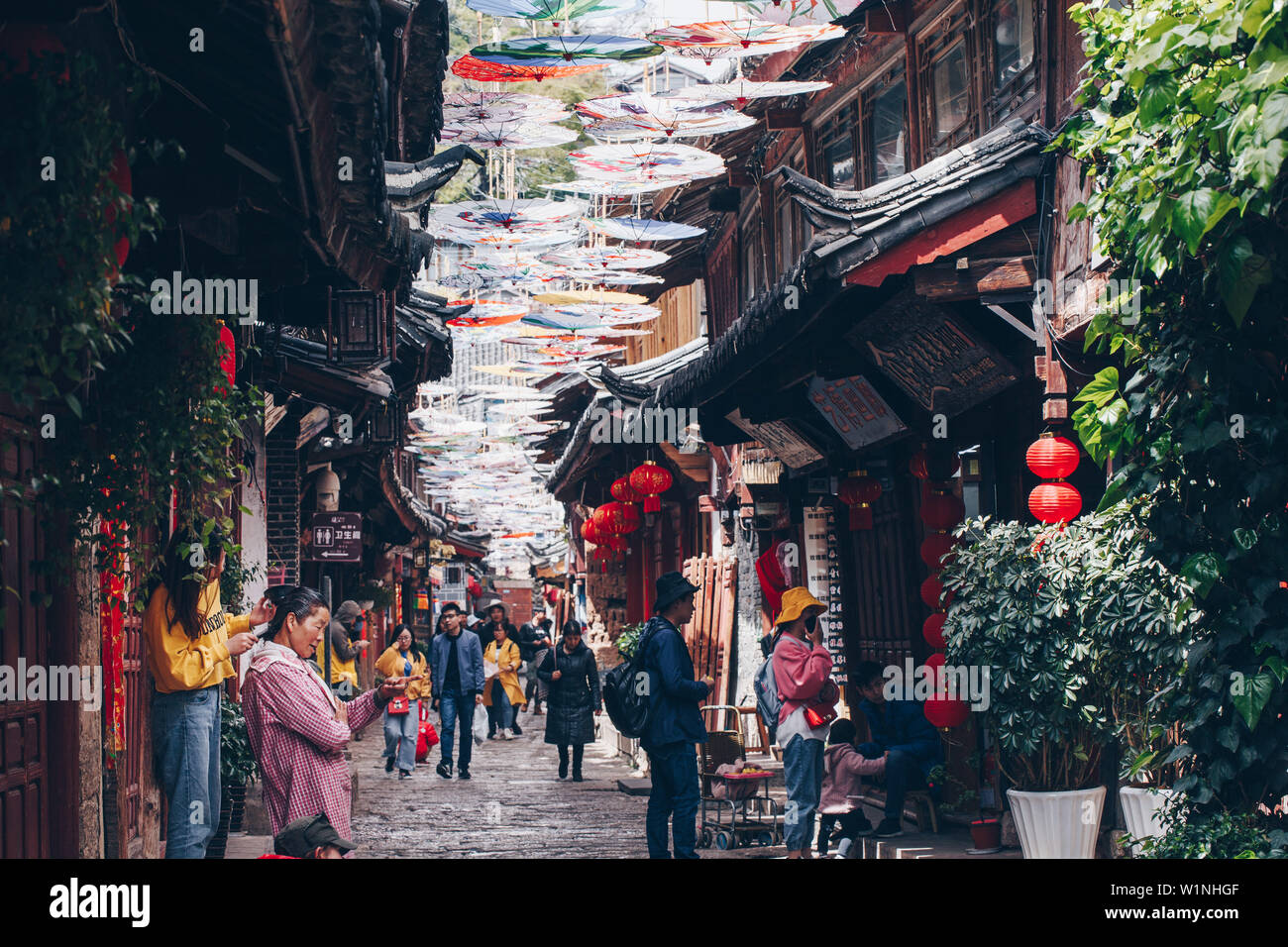 Daughter dyes her mother hairs on the busy umbrellas decorated street of ancient Lijiang town, Yunnan, China Stock Photo
