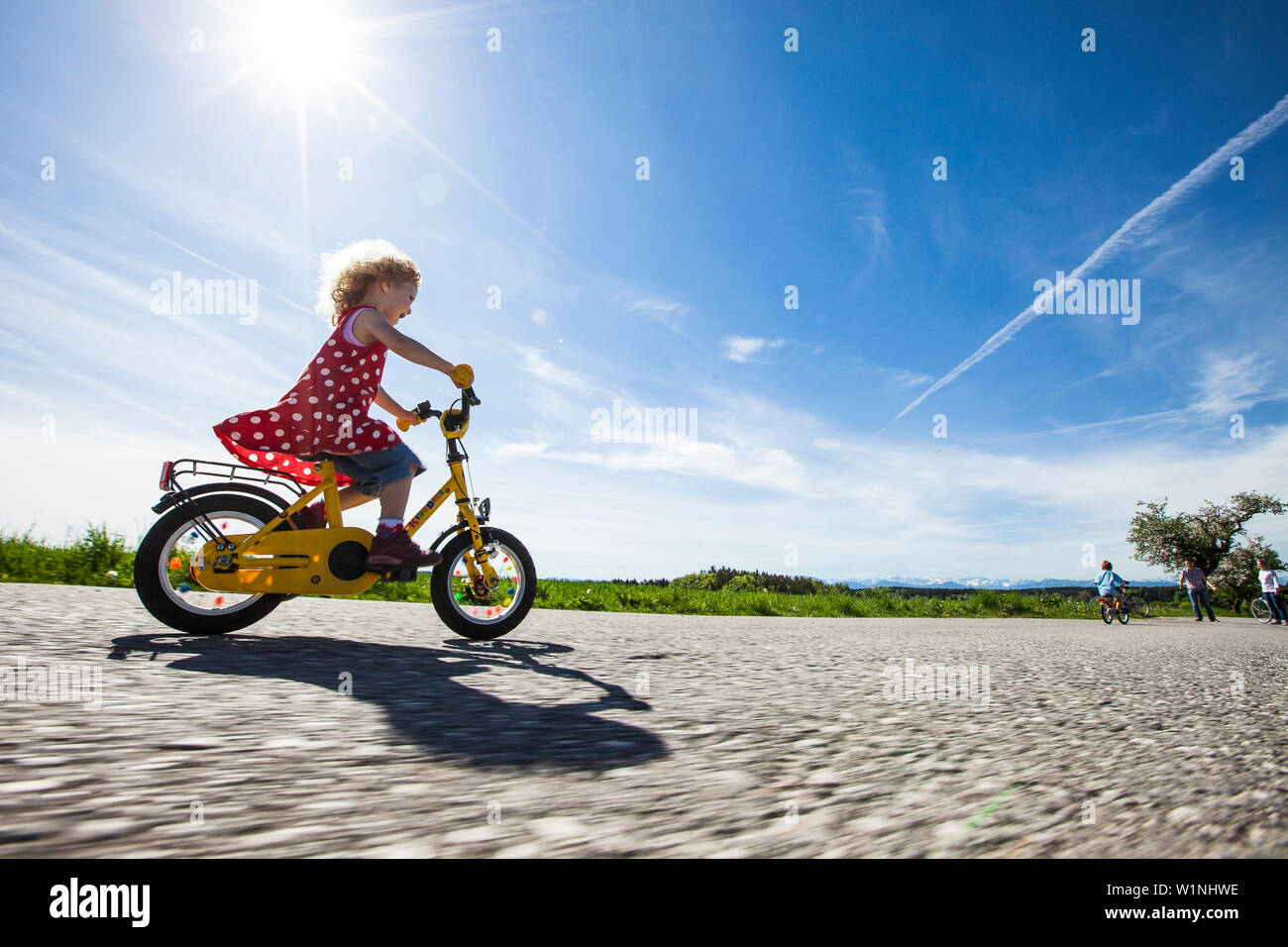 Children cycling, parents standing in background, Upper Bavaria, Germany Stock Photo