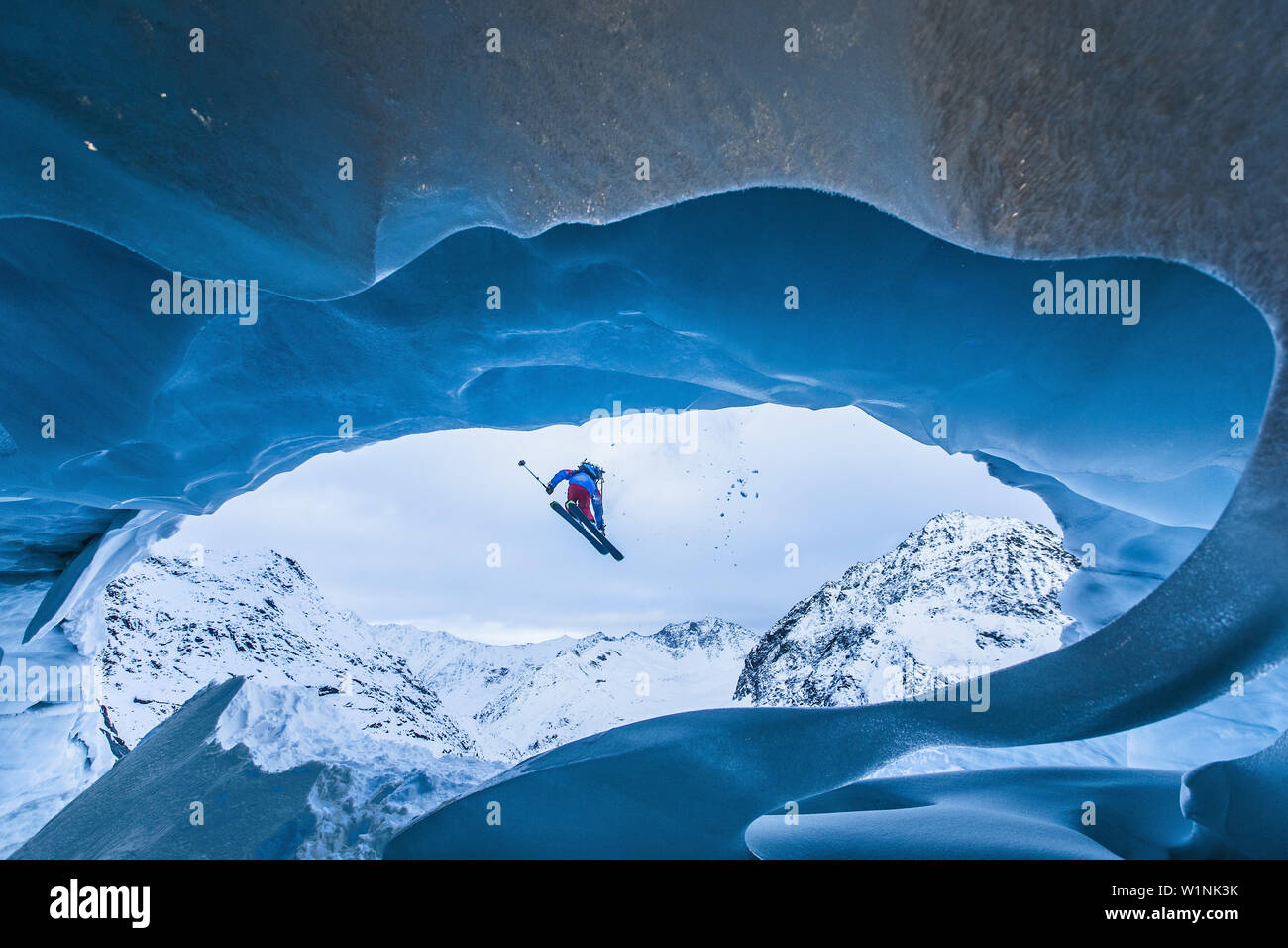 Young female freeskier jumping down from a cave of a glacier in the mountains, Pitztal, Tyrol, Austria Stock Photo