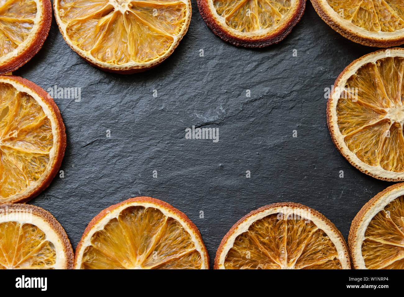 Bright slices of dried orange on a black slate texture board background, copy space. Stock Photo