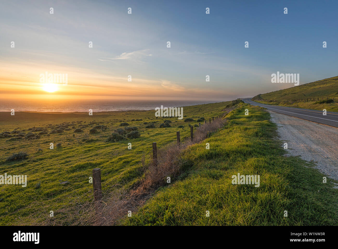 The Sun setting over the ocean with a meadow in the foreground. Big Sur, California, United States. Stock Photo