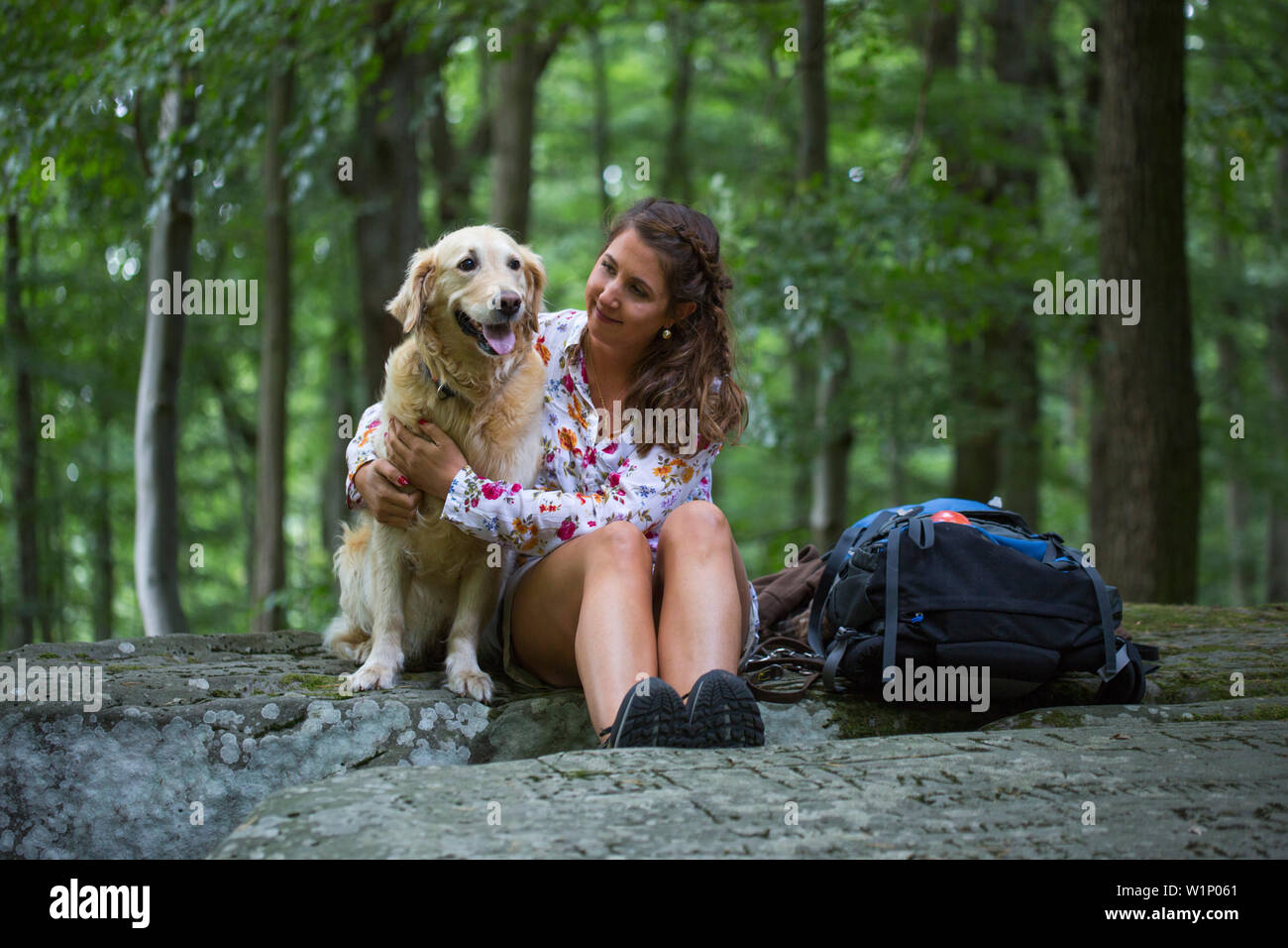 Young woman and Golden Retriever dog sit atop Lange Steine rock formation in Hessisches Kegelspiel mountains Stock Photo