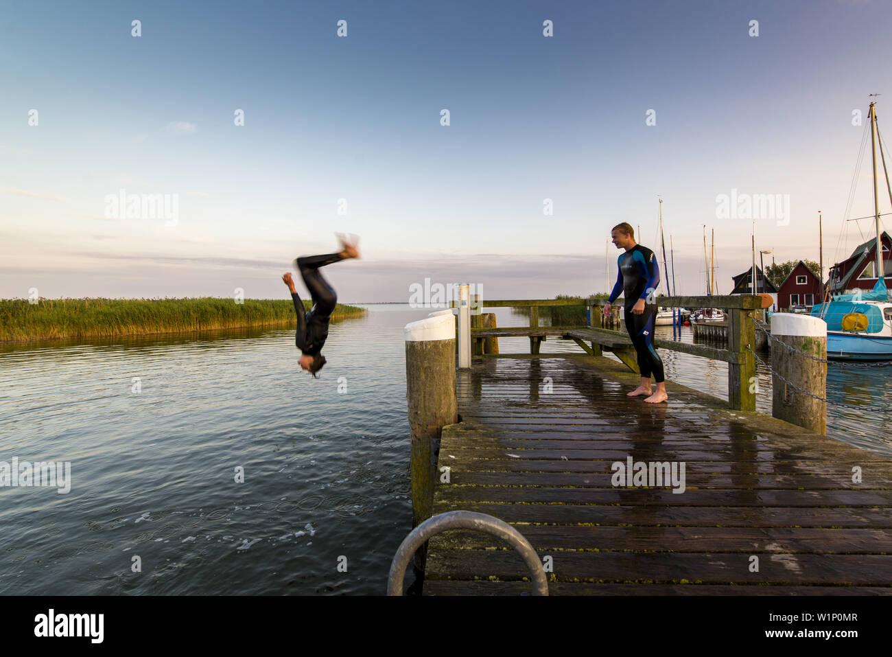 Three young people have fun and jump with a backflip from a pier in the Bodden by Ahrenshoop. Ahrenshoop, Althagen, Darß, Mecklenburg-Vorpommern, Germ Stock Photo