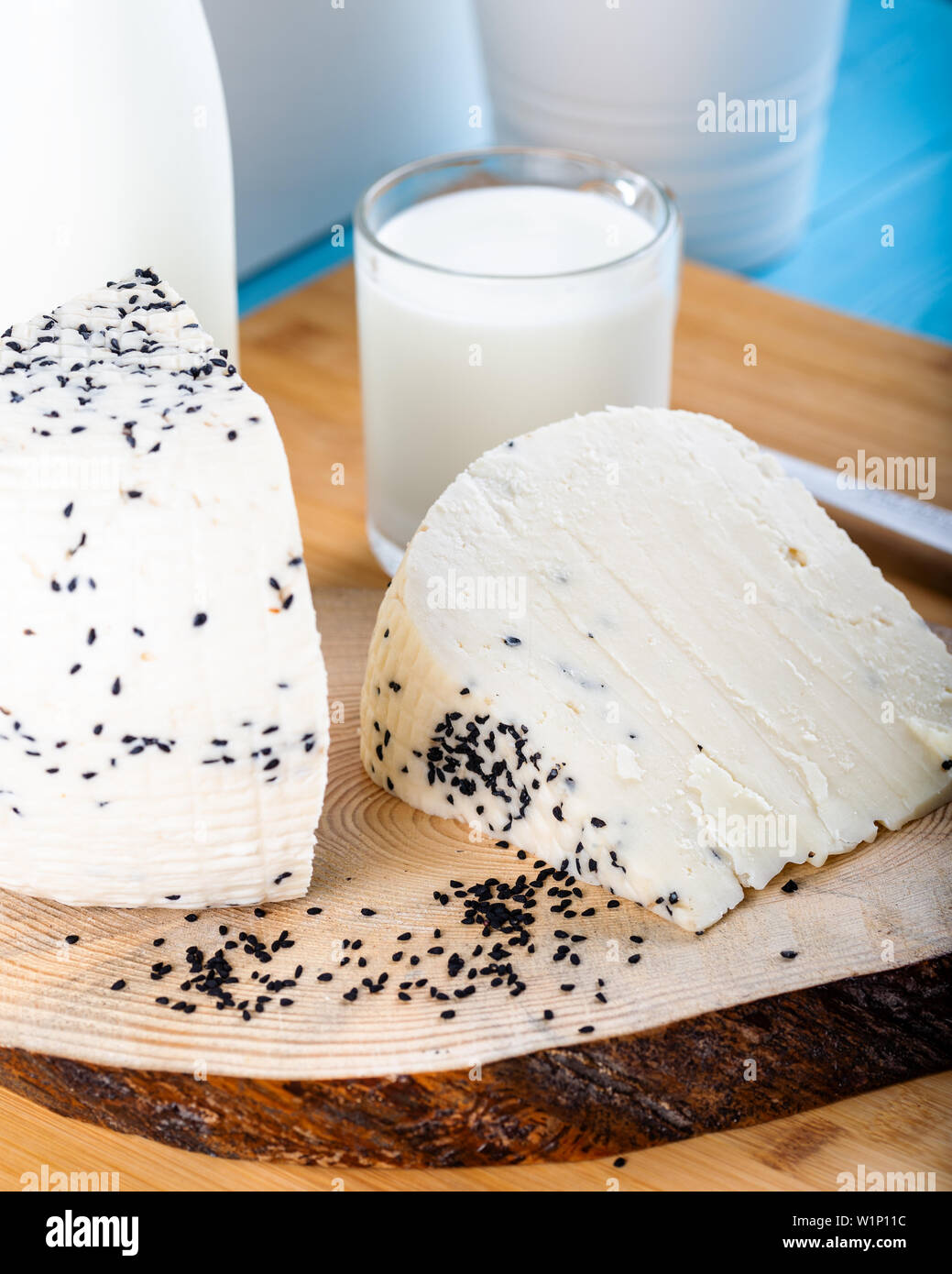 Cheese with black cumin seeds with bottle of milk on wooden background. Stock Photo