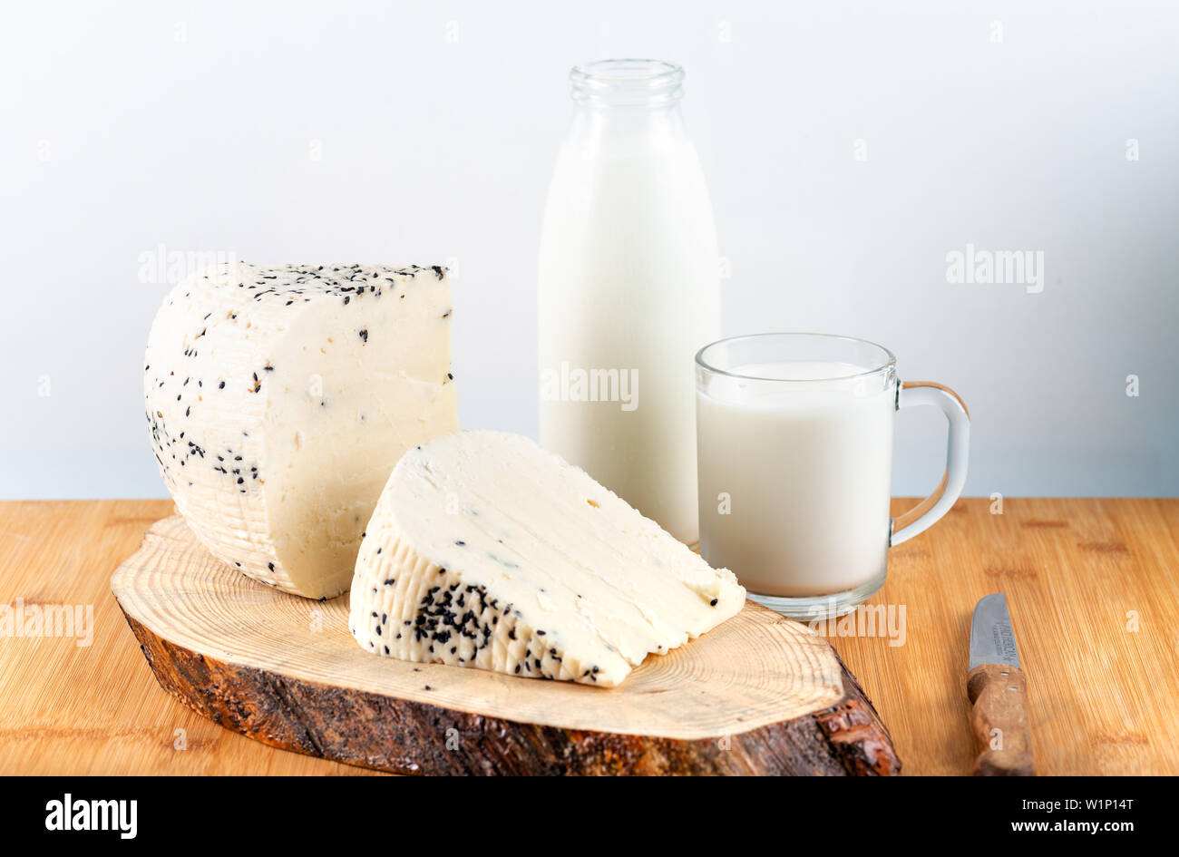 Cheese with black cumin seeds with bottle of milk on wooden background. Stock Photo