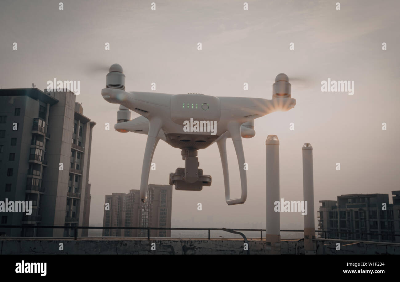 Back view of white quadcopter drone with attached camera filming at golden light. Stock Photo