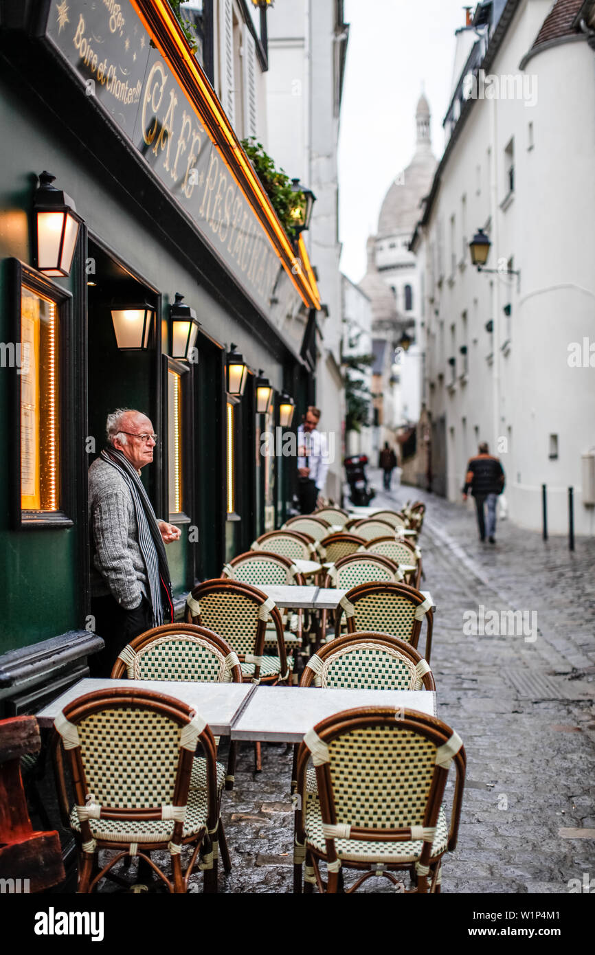 An old man smokes in front of the entrance to a restaurant and Basilica Sacre Coeur in Montmartre, Paris, France, Europe Stock Photo