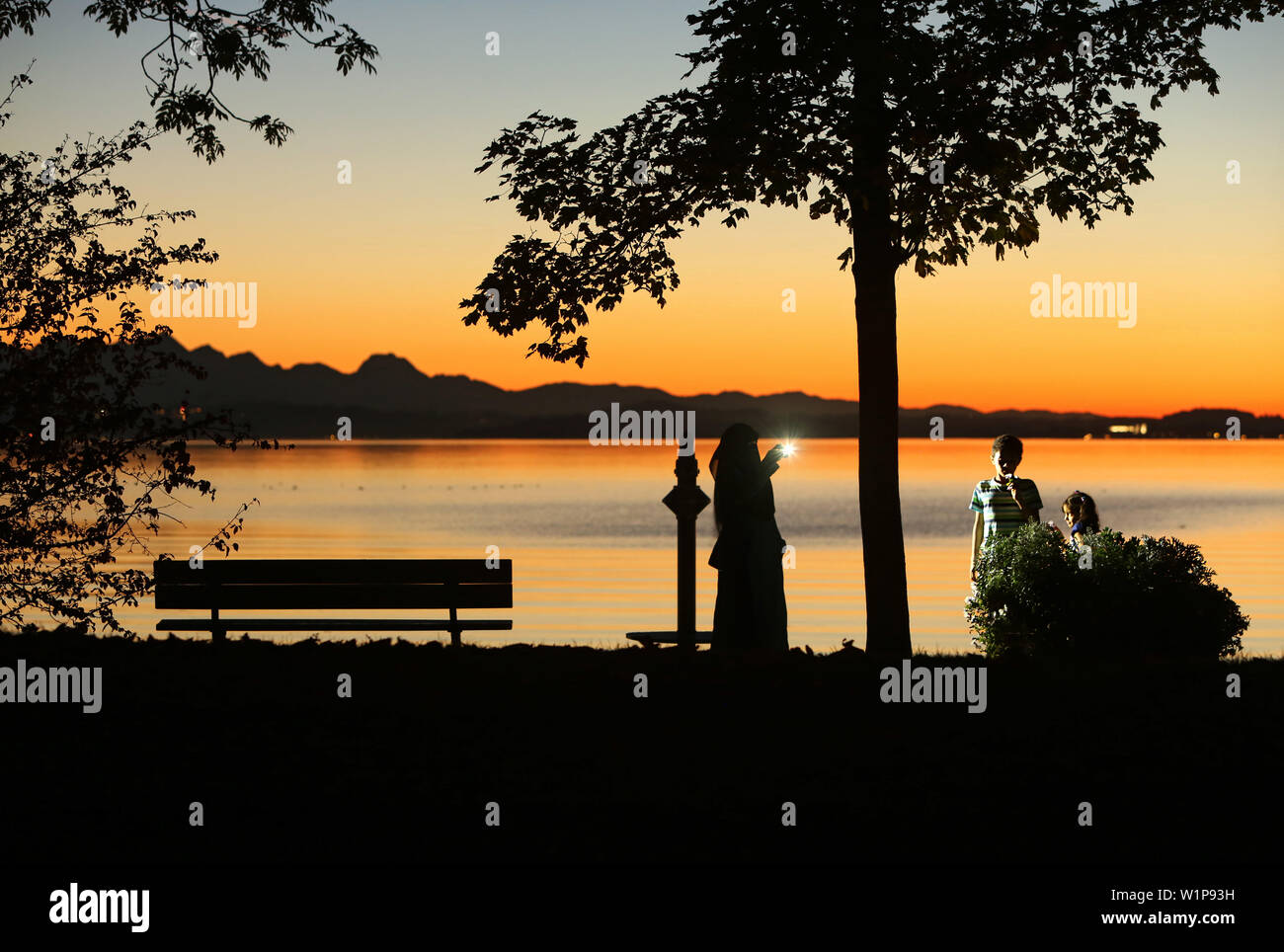 In the last evening light veiled woman makes a cell phone photo of your children on the banks of Lake Chiemsee Stock Photo