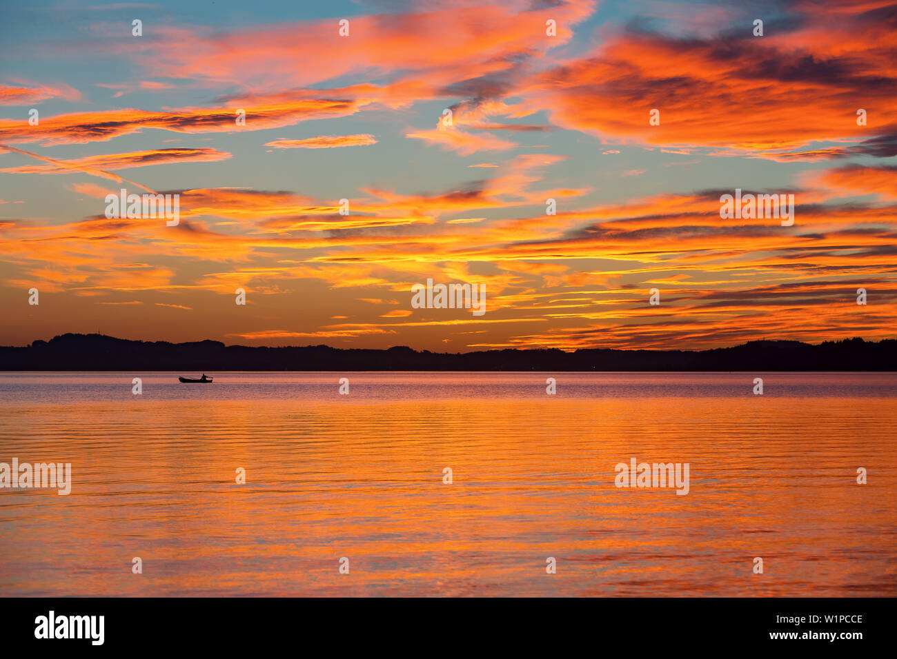 Anglers with small motor boat in the last evening light at sunset on Lake Chiemsee, dramatic color and clouds mood Stock Photo