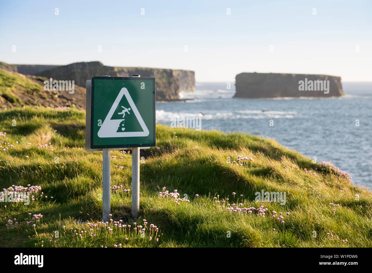 Danger! The edge of the cliff is not secured by fences or walls , and this sign warns walkers to watch their step, Kilkee, County Clare, Ireland, Euro Stock Photo