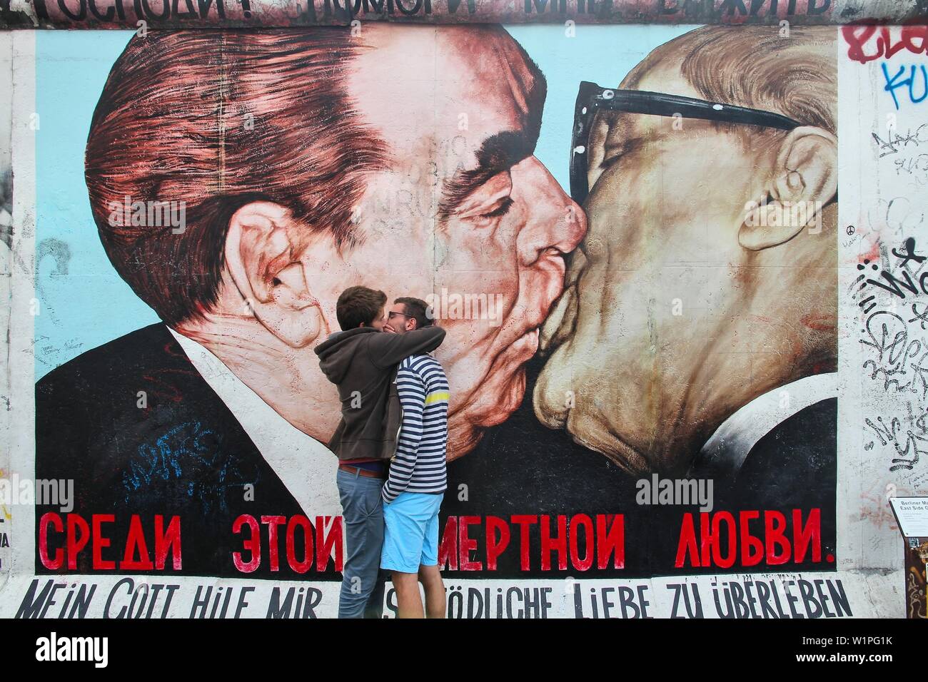BERLIN, GERMANY - AUGUST 26, 2014: Tourists pretend to reenact the kiss from Berlin Wall artwork. Part of former Berlin Wall is covered in art by more Stock Photo