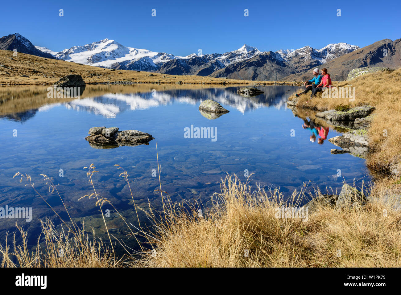 Man and woman sitting at mountain lake with Cevedale in background, valley of Martelltal, Ortler group, South Tyrol, Italy Stock Photo