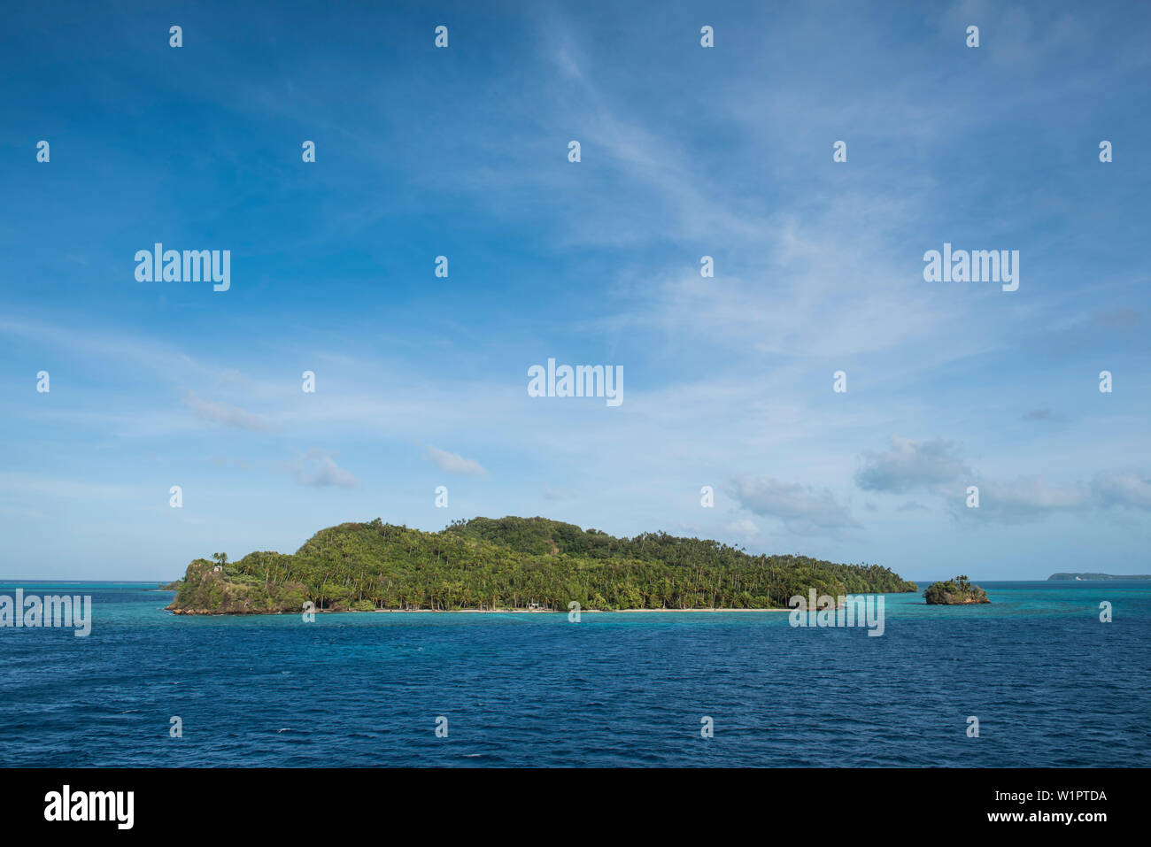 Small, tree-covered islands stand in turquoise water under a lightly clouded blue sky, Mata Utu, Uvea Island, Wallis and Futuna, South Pacific Stock Photo