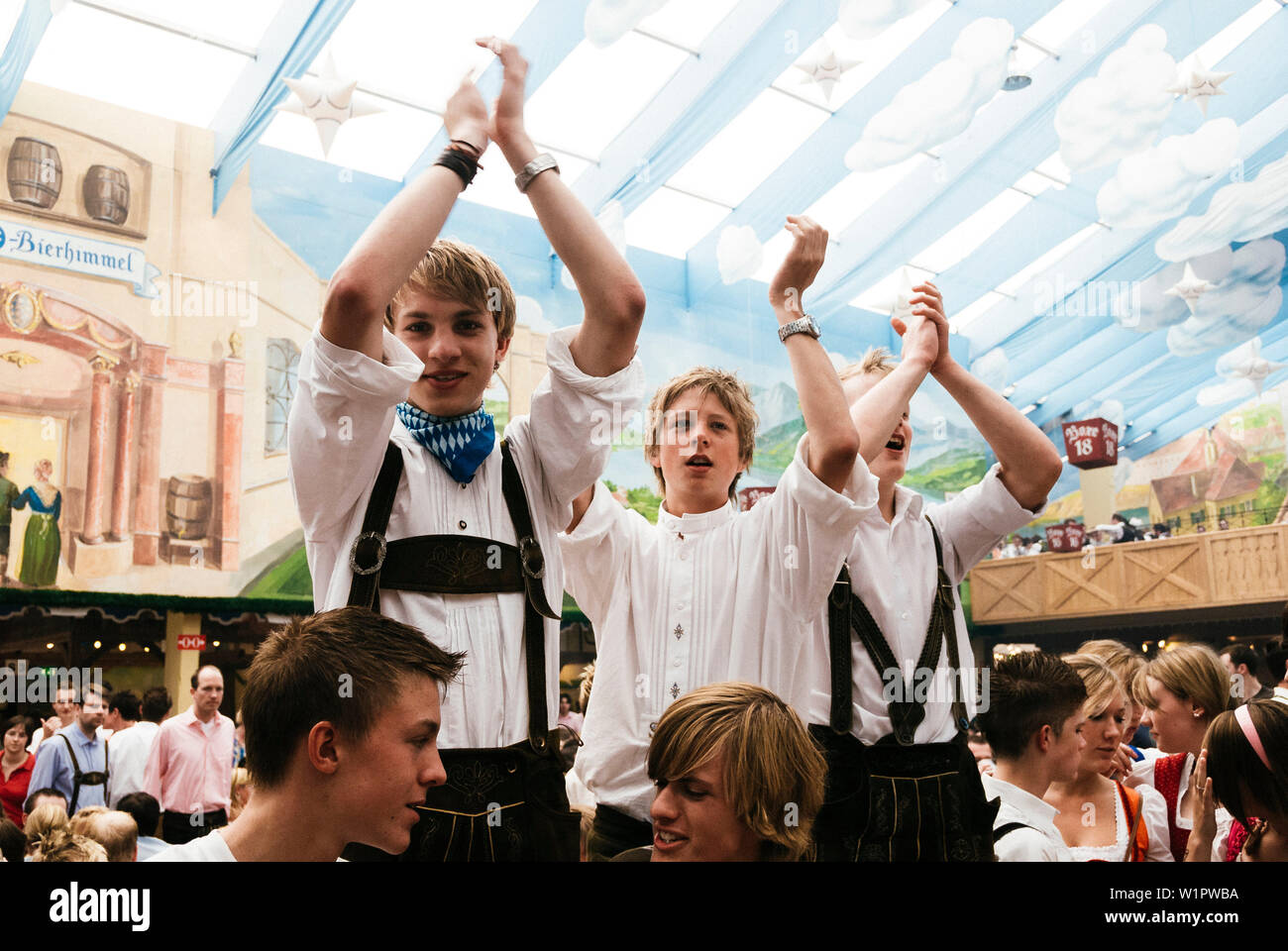 Young men in leather trousers standing on beer benches celebrate