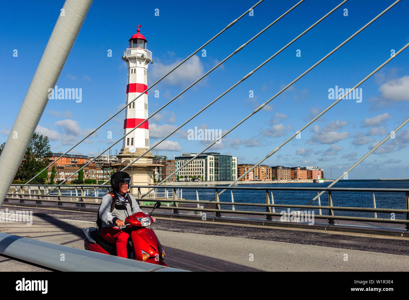 Red white lighthouse in sarnated harbor area, red scooter in foreground on a bridge, Malmo Southern Sweden, Sweden Stock Photo