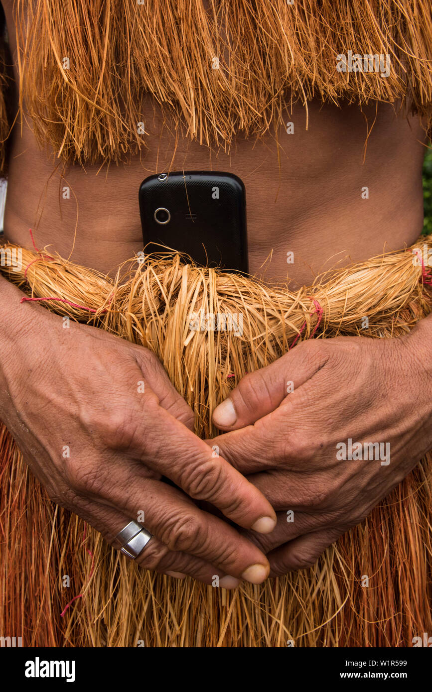 A member of the Witoto people (also Huitoto) carries a cell-phone tucked into the waist of his traditional apparel made of plant-fibers, Pebas (also P Stock Photo