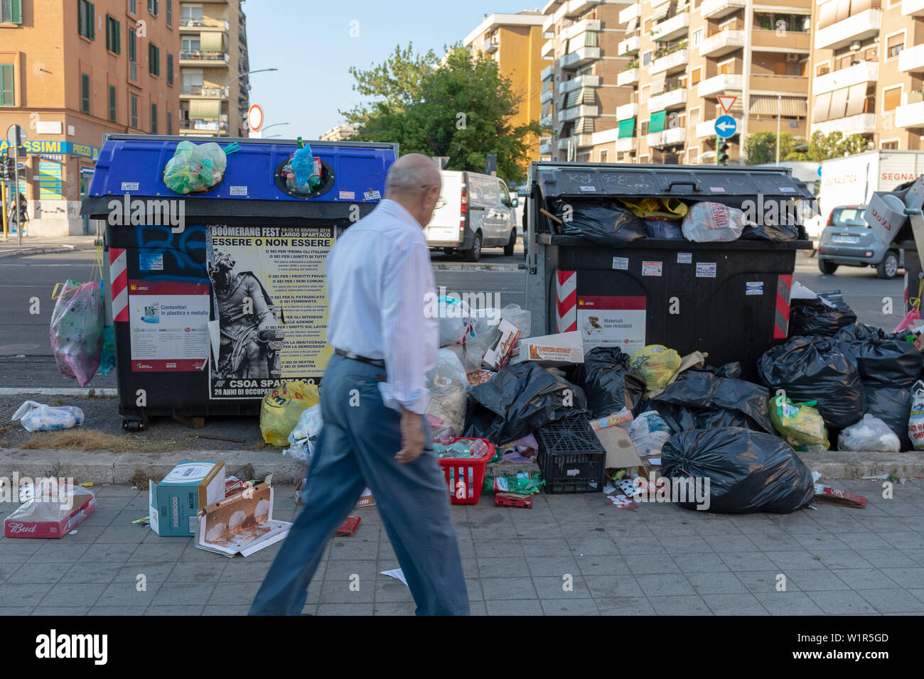 Rome, Italy - June 27, 2019: Garbage bins full of rubbish, among the streets and buildings of the city. A citizen looks at them in disbelief. Stock Photo