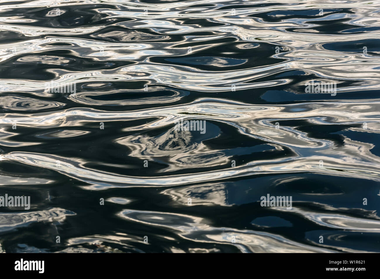 Abstract natural background of water texture with reflection of clouds in beautiful waves of dark water at sunset Stock Photo