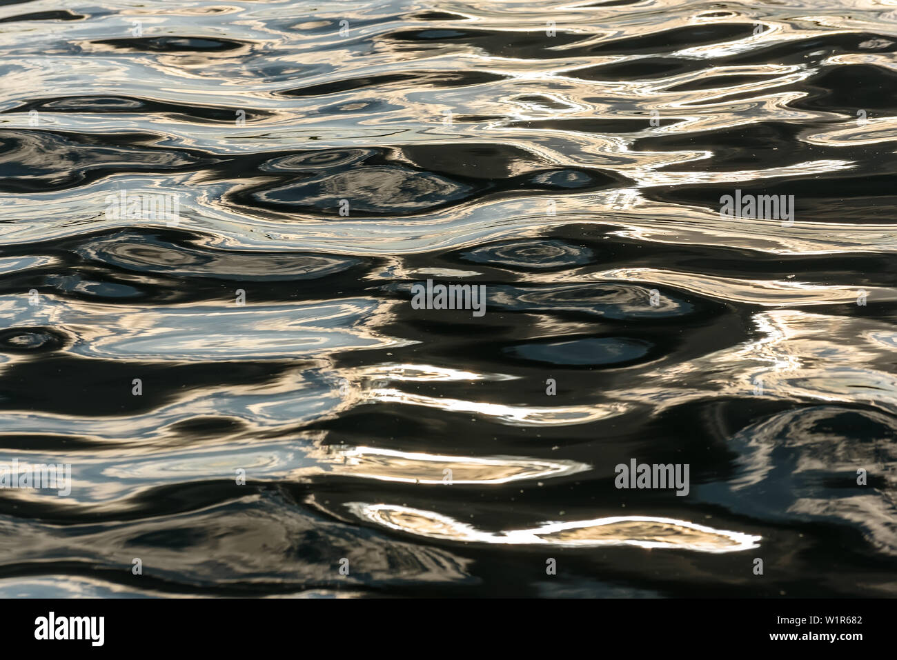 Abstract natural background of water texture with reflection of clouds in beautiful waves of dark water at sunset Stock Photo