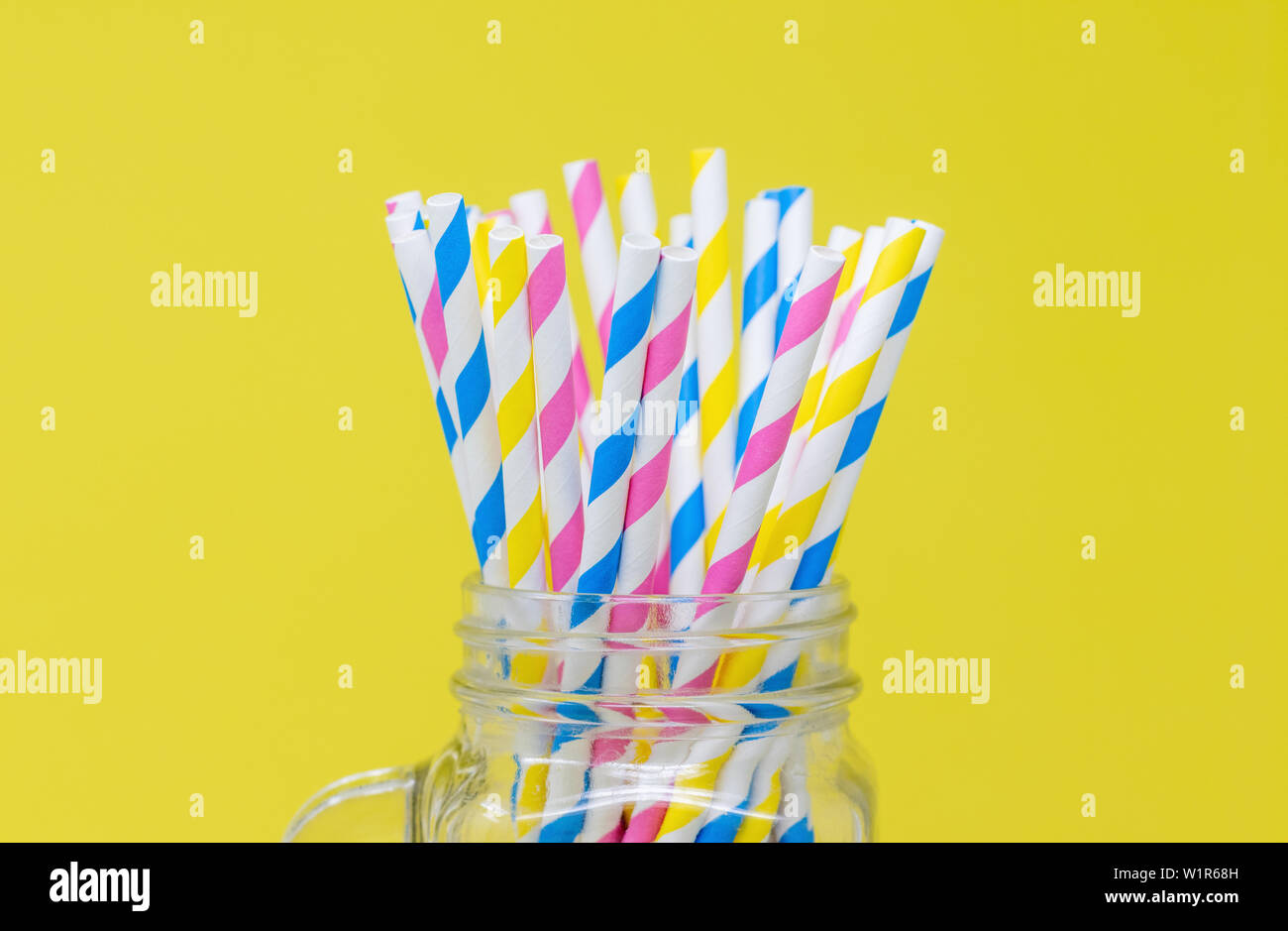 Colorful paper straws in a glass jar. with a yellow background. Closeup with a shallow depth of field. Stock Photo