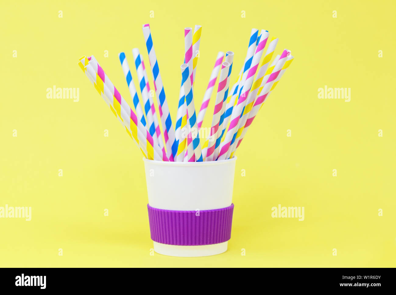 Paper straws in a reusable cup, against a yellow background Stock Photo