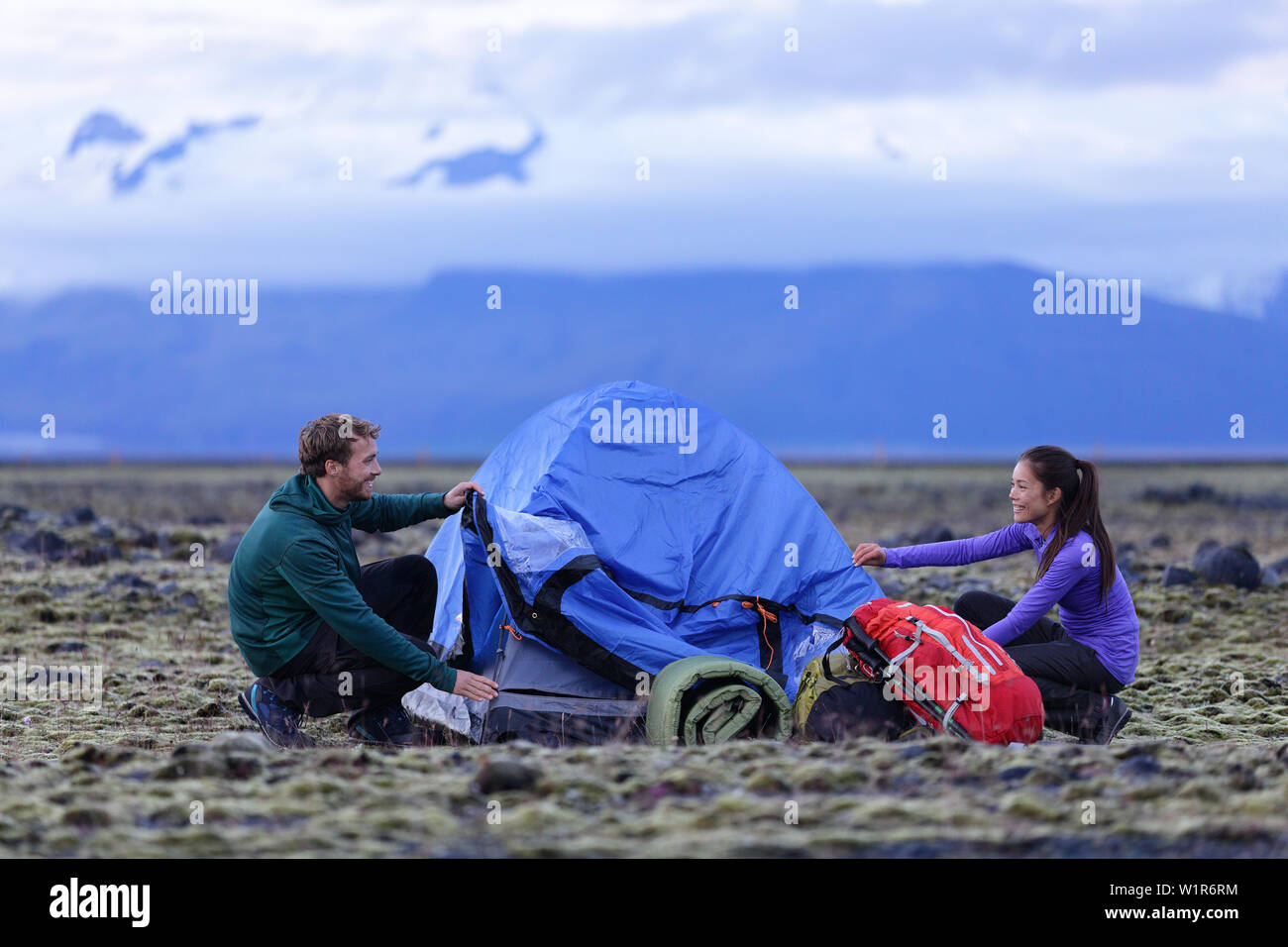 Tent people pitching tent on Iceland at dusk. Couple setting up camp