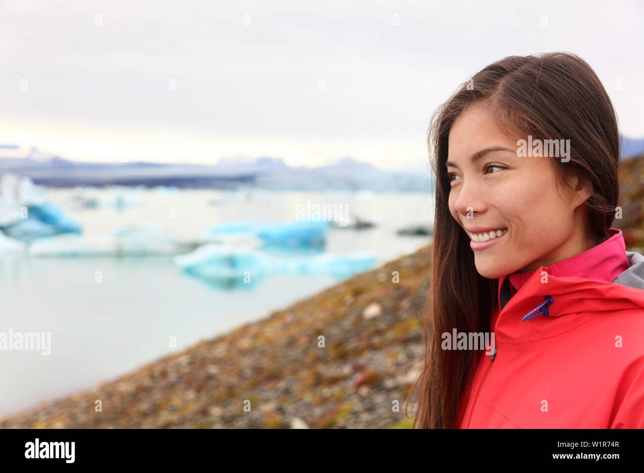 Woman at glacier lagoon on Iceland. Happy tourist woman looking enjoying view of Jokulsarlon glacial lake. Smiling woman in beautiful Icelandic nature landscape looking at iceberg. Stock Photo