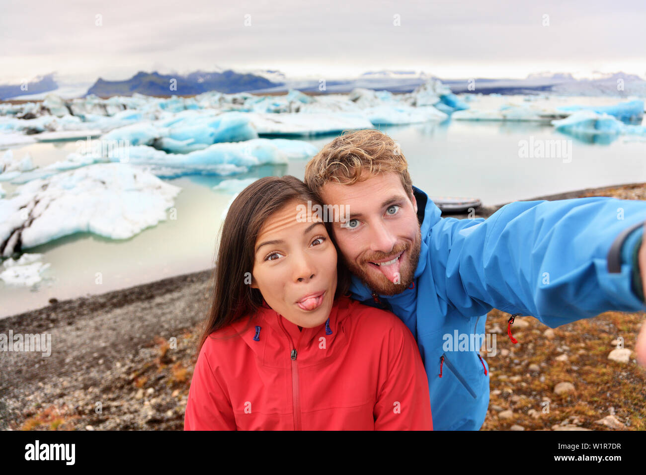 Funny selfie couple taking self portrait photograph on Iceland having fun on travel by Jokulsarlon glacial lagoon / glacier lake. Tourists enjoying beautiful Icelandic nature landscape Vatnajokull. Stock Photo