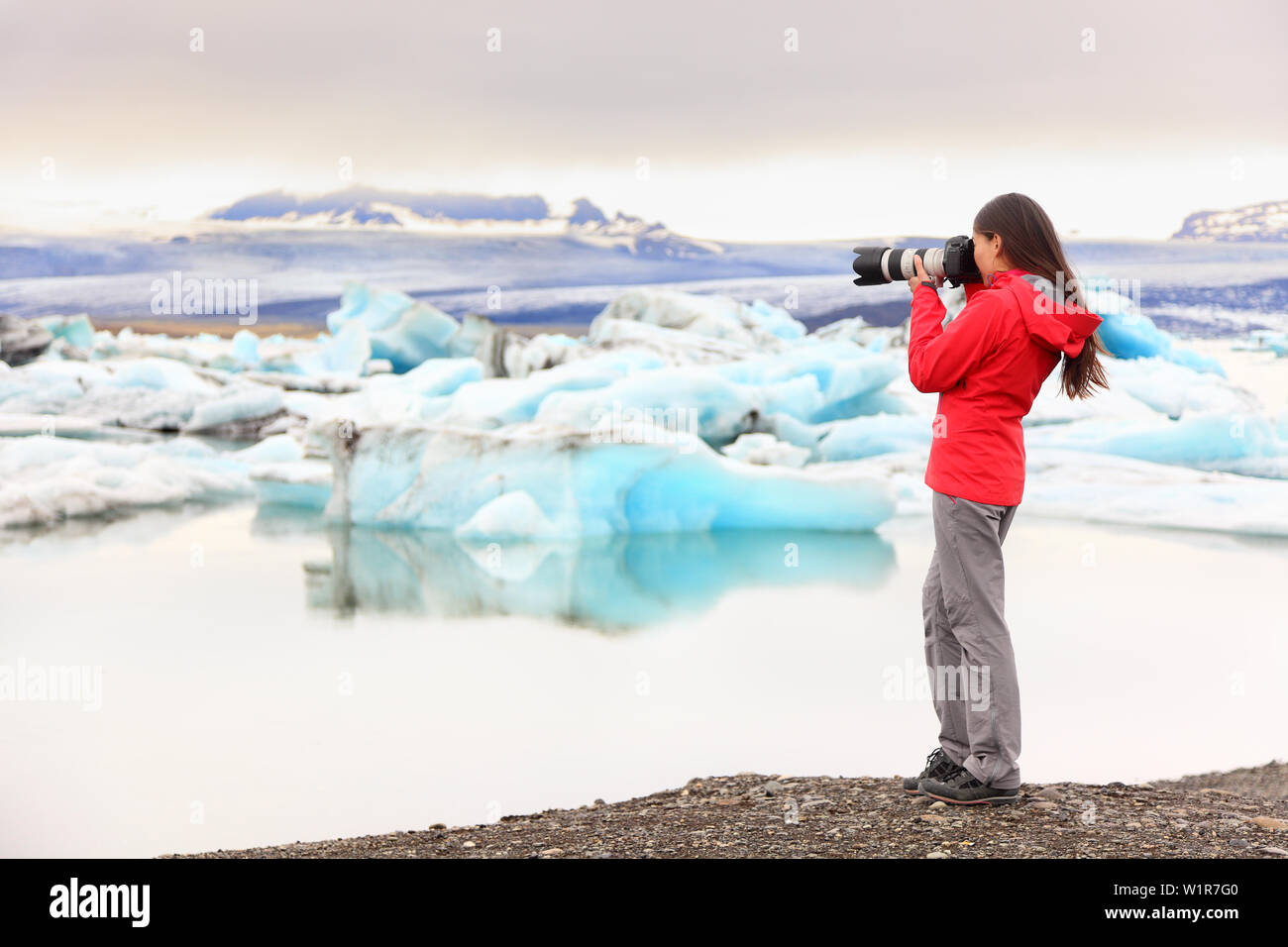 Nature landscape photographer taking picture photos with SLR camera on Iceland Jokulsarlon glacial lagoon / glacier lake. Woman taking photograph of beautiful Icelandic nature with Vatnajokull. Stock Photo