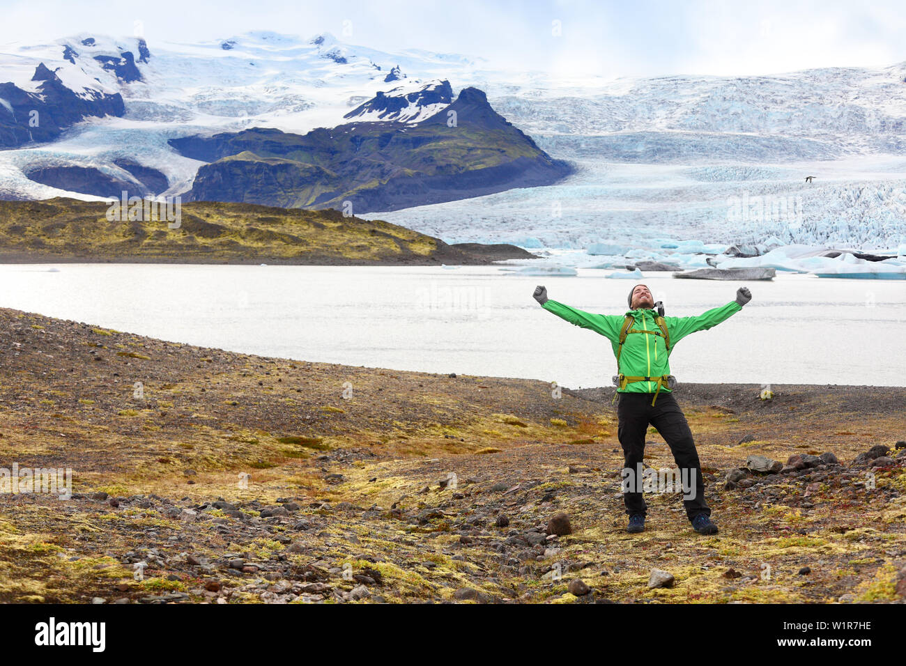 Hiking adventure travel man cheering happy on hike on Iceland. Hiker cheerful at glacier and glacial lagoon / lake of Fjallsarlon, Vatna glacier, Vatnajokull National Park. Icelandic nature landscape. Stock Photo