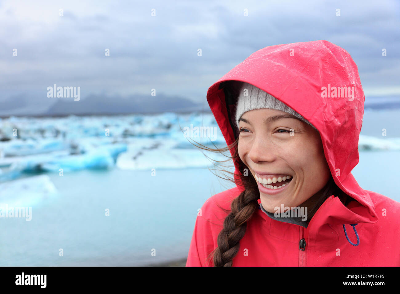 Outdoors Woman in hardshell raincoat jacket at glacier lagoon on Iceland. Happy smiling tourist girl enjoying view of Jokulsarlon glacial lake beautiful Icelandic nature landscape with icebergs. Stock Photo